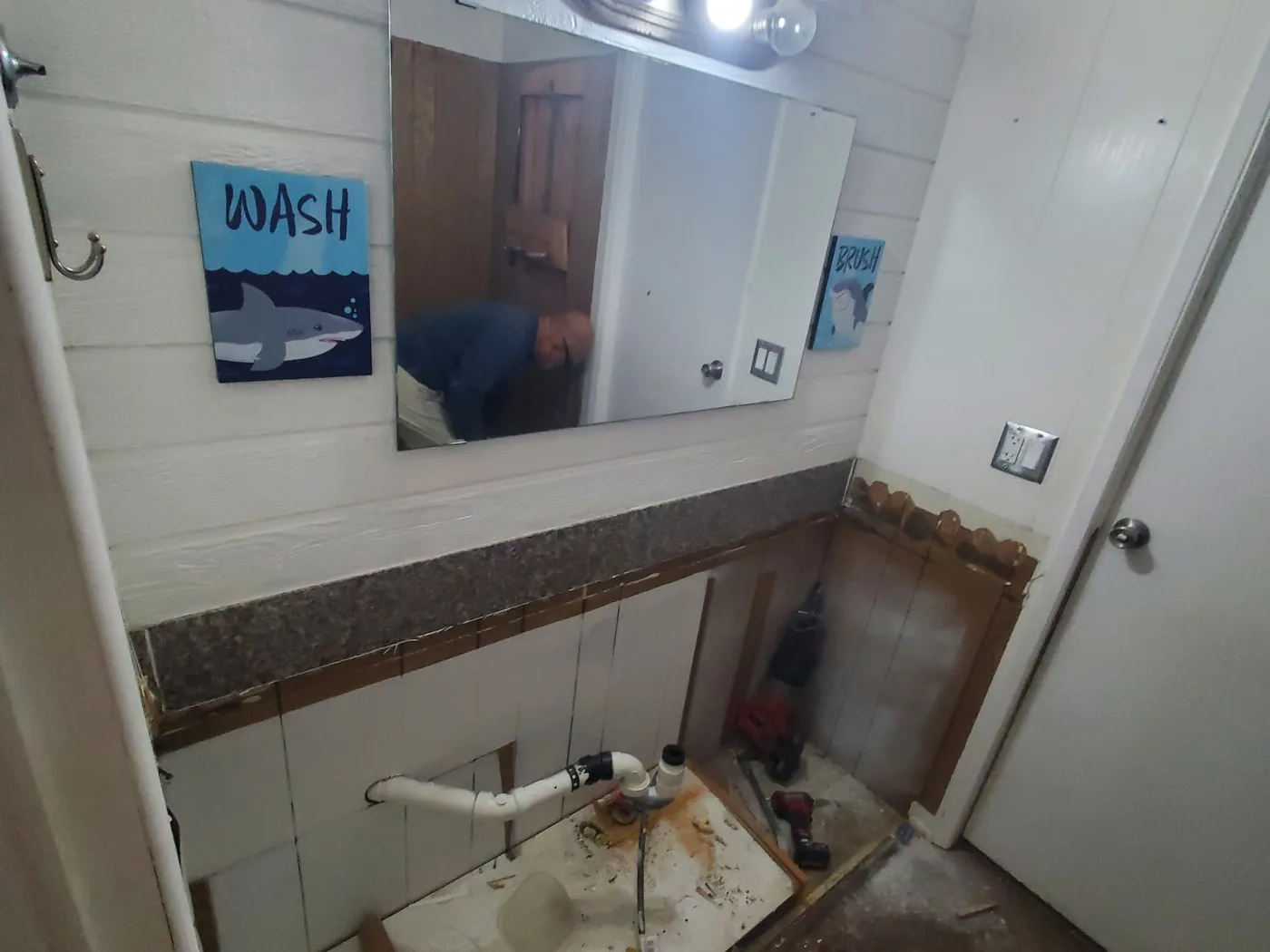 Before: Gutted bathroom wall with exposed plumbing and torn-out flooring